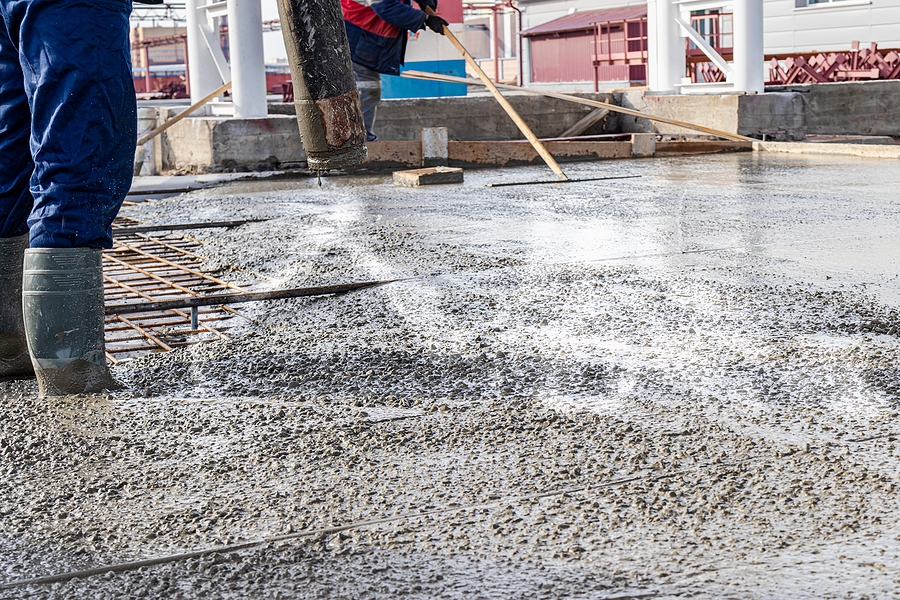 Closeup of a worker wearing boots and standing in concrete during a concrete pour at a construction site.