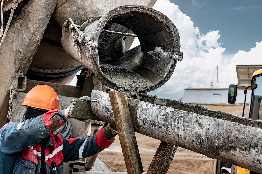 Closeup of a concrete mixing truck with a construction worker on site.