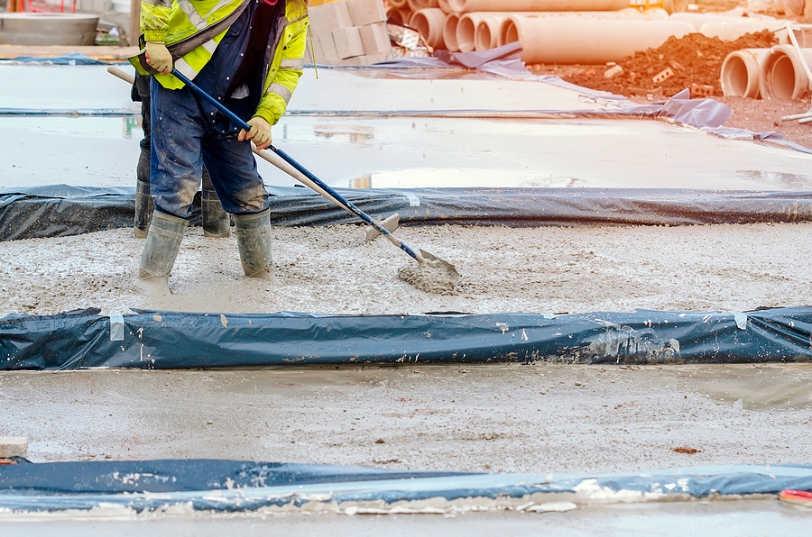 Closeup of a construction worker pouring and leveling concrete at a construction site.